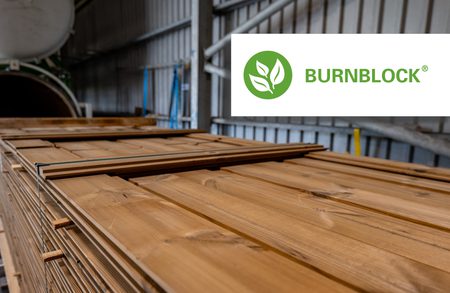Stacked wooden planks in an industrial lumber warehouse; a white Burnblock logo sits in the upper-right corner.