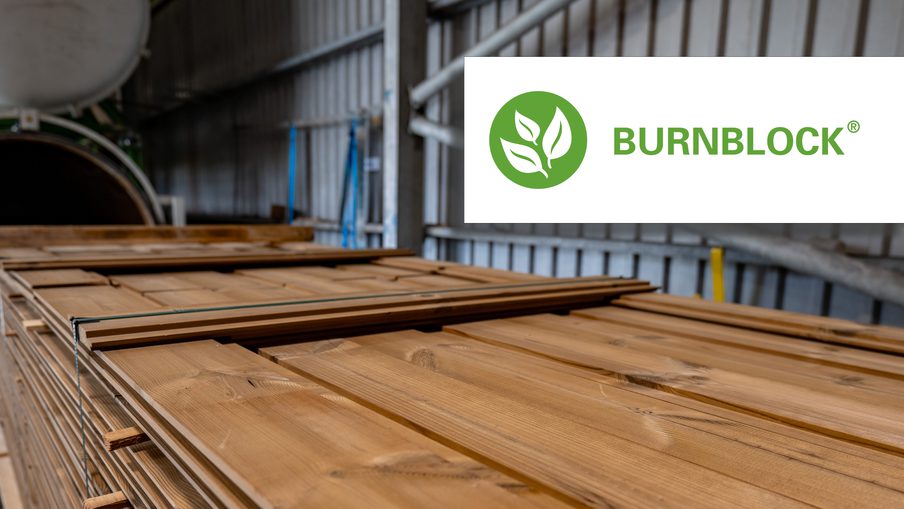 Stacked wooden planks in an industrial lumber warehouse; a white Burnblock logo sits in the upper-right corner.
