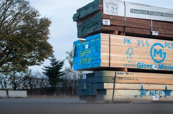 Stacks of lumber on pallets outdoors, blue-painted boards marked SUPER PRIME, with Hawkeye Forest Products banner and trees in the background.