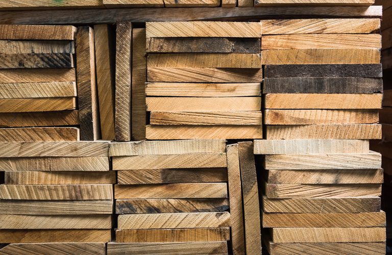 Stacked wooden planks in varying widths and brown tones, revealing grain patterns and rough edges in a dense lumber pile.