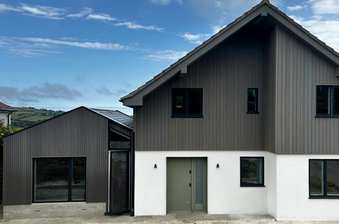 A modern house in Dorset, on the south coast of England, featuring Thermo-Ayous timber cladding in 'stone grey' with black-framed windows and a green front door.