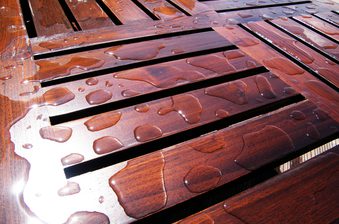 Close-up of glossy, reddish-brown wooden slats with scattered water droplets on a wet surface.