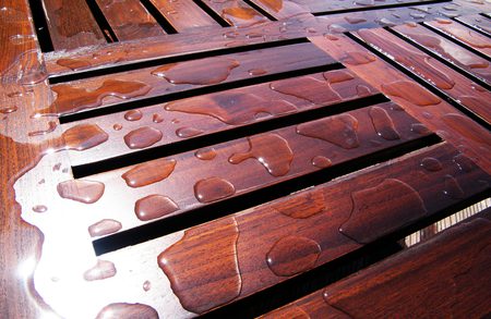 Close-up of glossy, reddish-brown wooden slats with scattered water droplets on a wet surface.