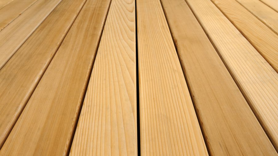 Close-up of parallel wooden deck boards with visible grain, warm honey-brown color, and narrow gaps between them.