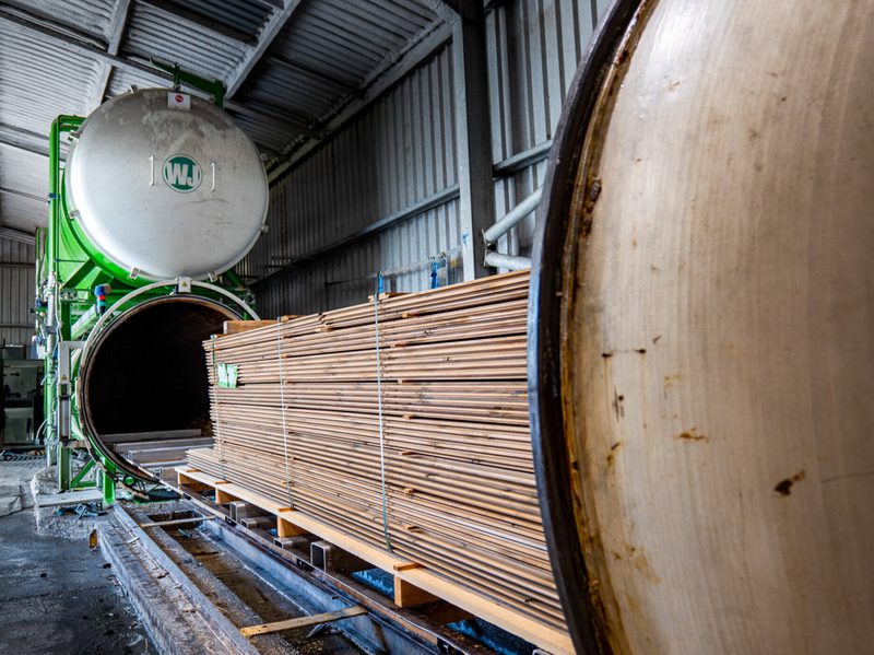 Industrial workshop with a large green machine and an open circular tunnel; a pallet of bundled wooden planks sits beside it.