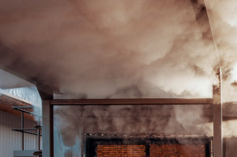Smoke-filled interior of an industrial space with exposed brick wall, metal beams, and a blue-tinted wall on the left.