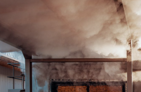 Smoke-filled interior of an industrial space with exposed brick wall, metal beams, and a blue-tinted wall on the left.