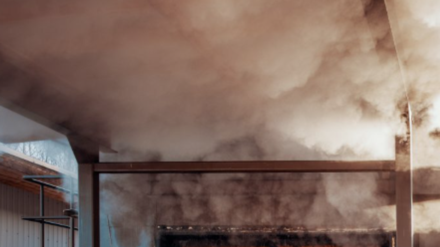 Smoke-filled interior of an industrial space with exposed brick wall, metal beams, and a blue-tinted wall on the left.