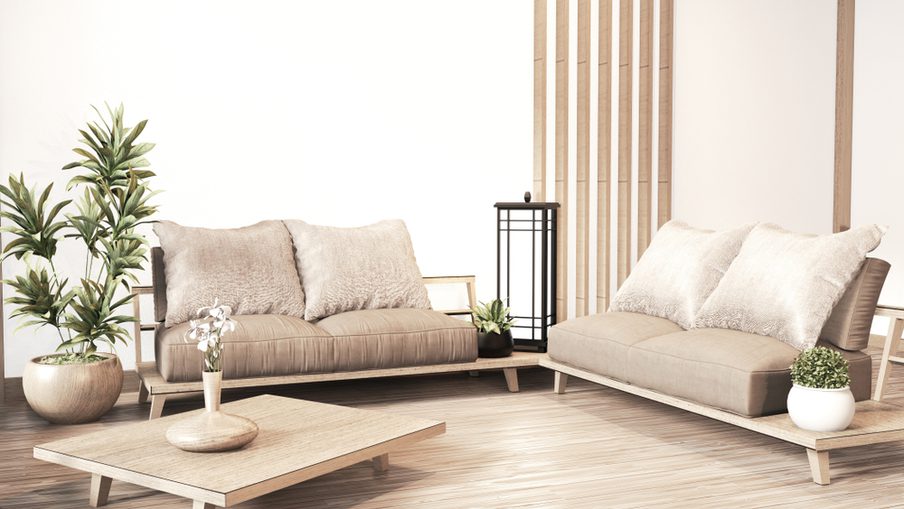 Minimalist living room with two beige cushioned sofas on a wooden platform, a low coffee table, potted plants, a lantern, and a wooden slat divider.