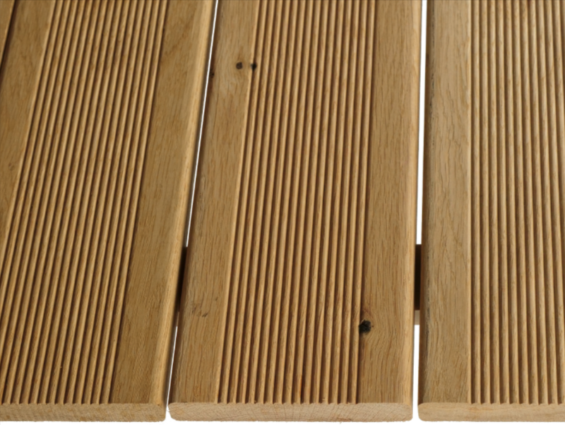 Close-up of light brown wooden slats with narrow grooves running along their length, resembling a slatted outdoor deck or bench.