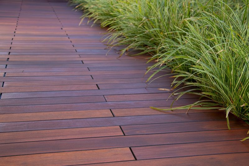 A wooden deck with reddish-brown planks extends into the distance, bordered by tall green ornamental grasses on the right.