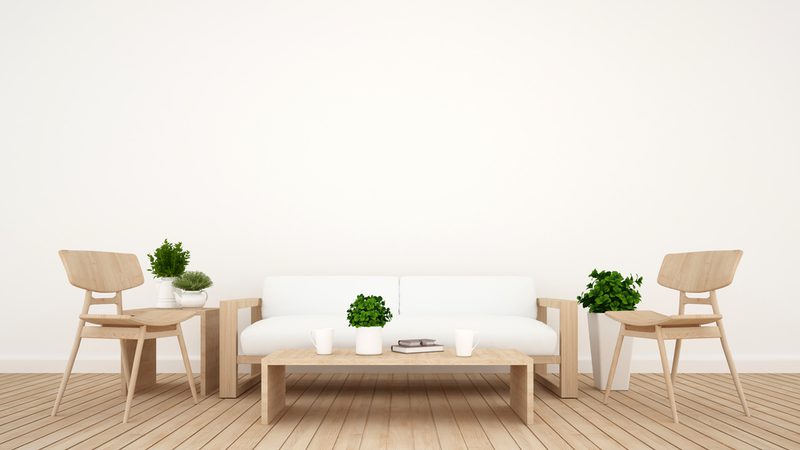 Minimalist living room with a white sofa, light wood chairs, a wooden coffee table, and potted plants; cups and books on the table.