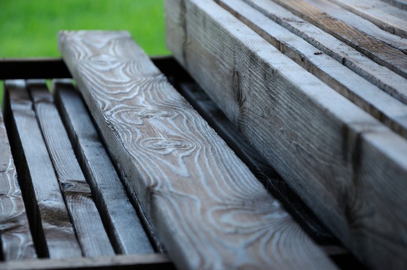 Close-up of weathered wooden boards with pronounced grain, stacked together, with a blurred green background.