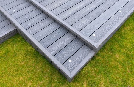 Top-down view of a gray composite deck with two-tier steps and wood-grain planks, silver screws, bordered by green grass.