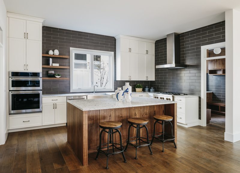 Bright modern kitchen with white cabinets, dark gray subway tile backsplash, marble-topped wooden island, and four metal-and-wood stools.