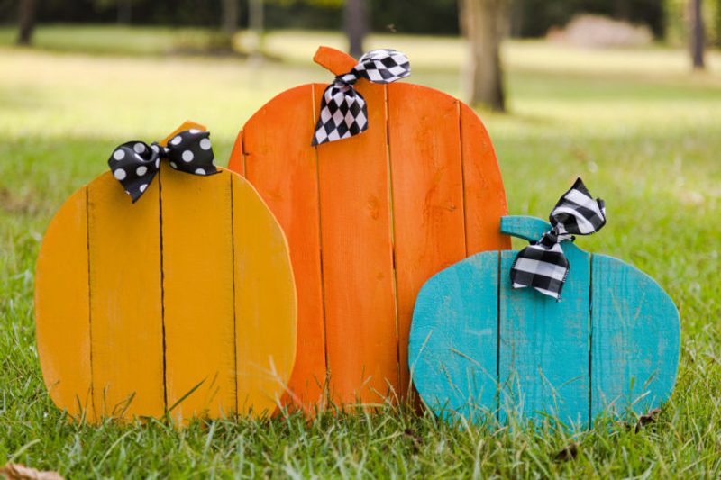 Three colorful wooden heart shapes (yellow, orange, turquoise) with black-and-white bows sit on a grassy park lawn.
