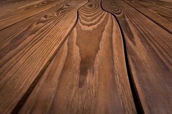 Close-up of warm brown wooden planks with pronounced grain, knots, and narrow gaps, resembling a deck or wooden table surface.