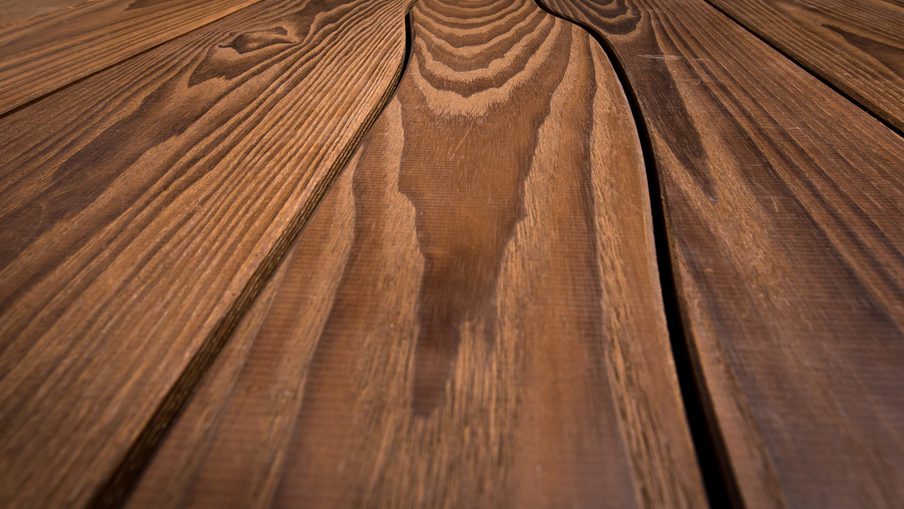 Close-up of warm brown wooden planks with pronounced grain, knots, and narrow gaps, resembling a deck or wooden table surface.