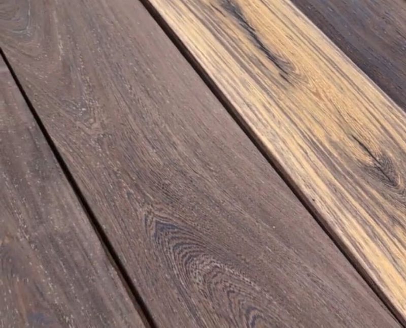 Close-up of weathered wooden deck boards with dark brown grain, lighter tan streaks, and narrow gaps between the planks.
