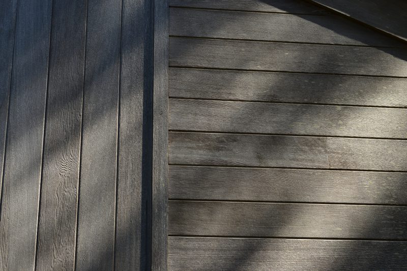 Two-toned wooden deck with vertical dark planks on the left and horizontal lighter planks on the right, lit by sunlight with soft shadows.