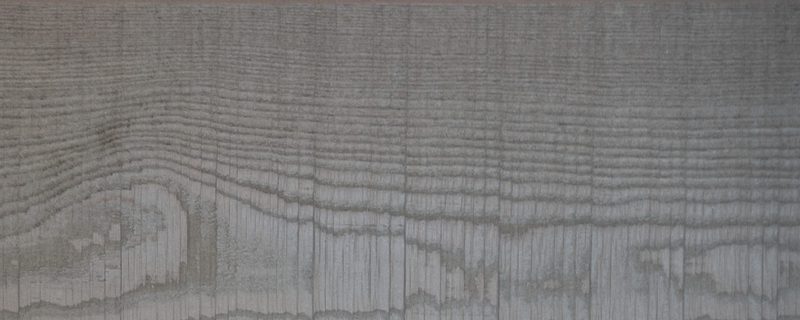 Close-up of a weathered grey wooden surface with pronounced horizontal grain lines and subtle darker streaks.