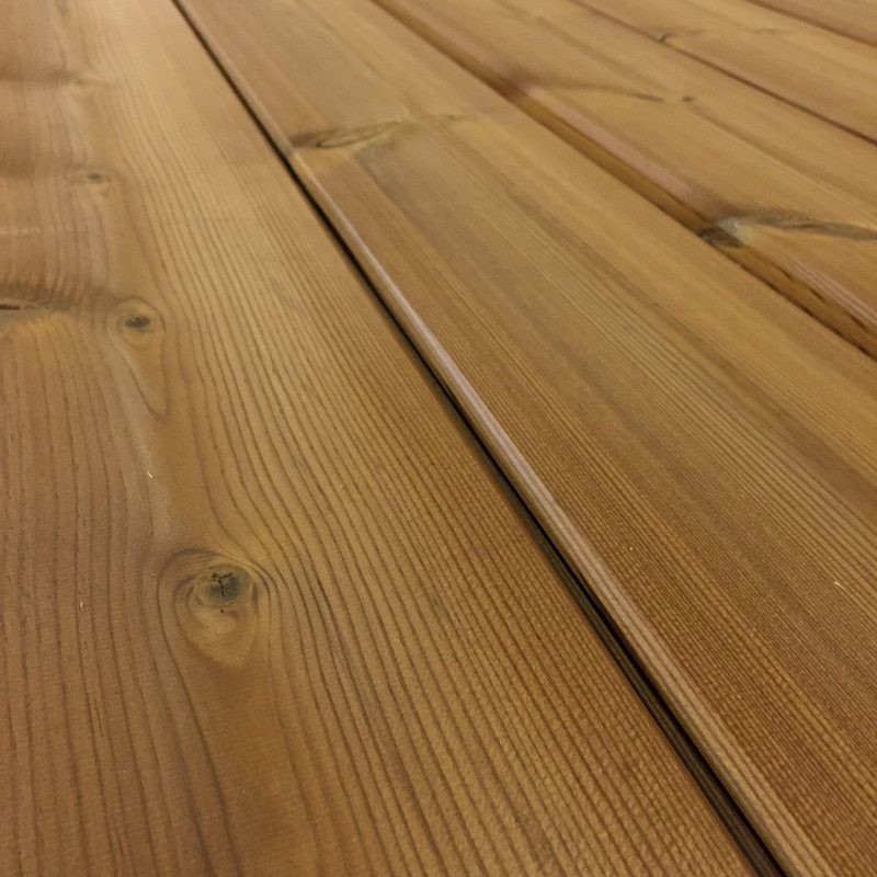 Close-up of warm brown wooden deck planks with visible grain patterns and knots, featuring a seam running between the boards.