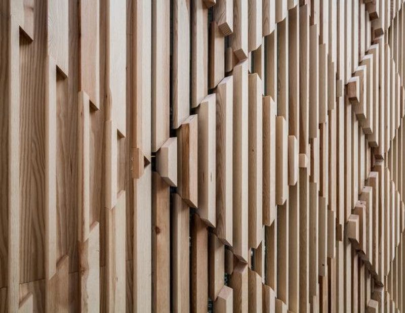Close-up of a light wood wall with vertical slats arranged in a repeating, three-dimensional geometric pattern of staggered blocks.