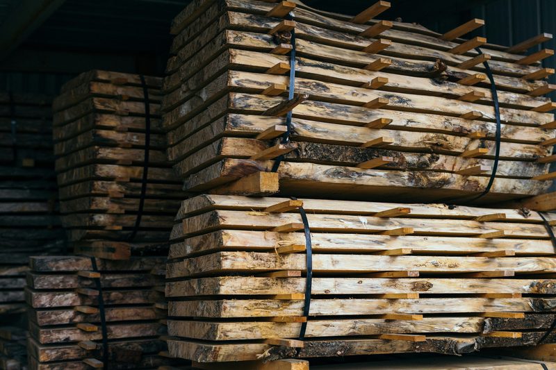 Stacks of weathered, rough-cut lumber bound with black straps, stored in a dim warehouse.
