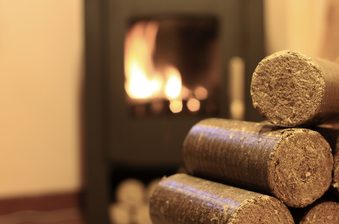 Stack of rough-cut wooden logs in the foreground, with a warm, blurred fireplace glow in the background.