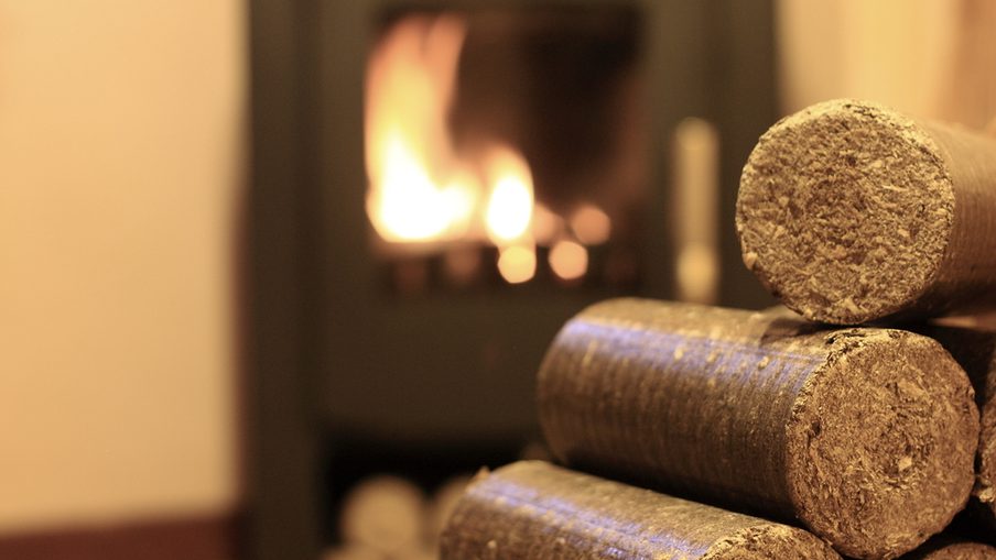 Stack of rough-cut wooden logs in the foreground, with a warm, blurred fireplace glow in the background.