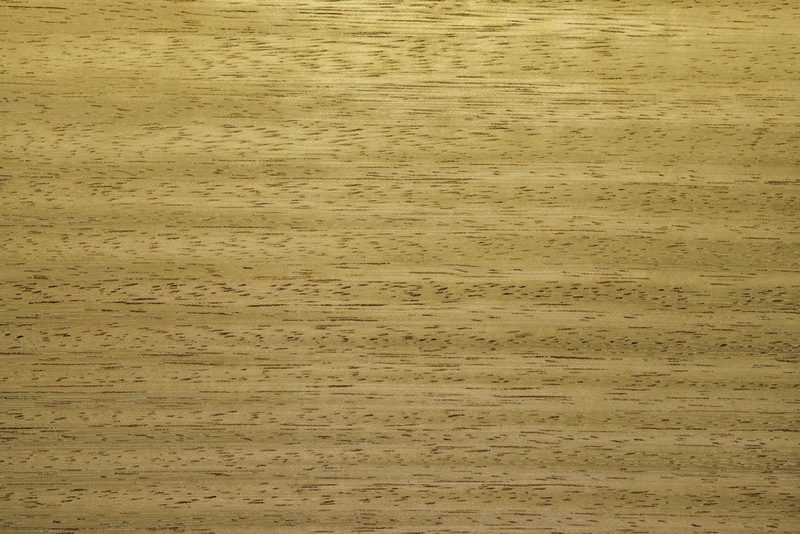 Close-up of a light brown wood surface with visible grain patterns and subtle dark streaks.