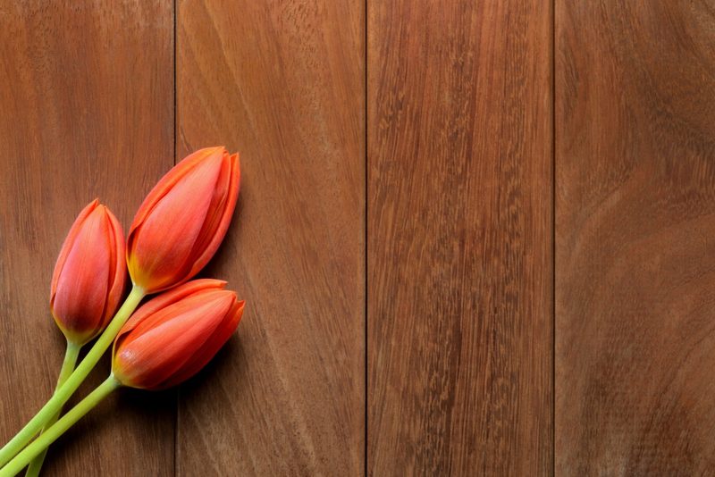 Three orange tulips with green stems lay diagonally on a brown wooden plank surface, occupying the left side of the frame.