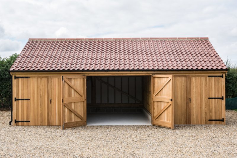 Wooden garden shed with a red-tiled roof and three bays; center bay open showing interior framing, outer bays closed, gravel ground.