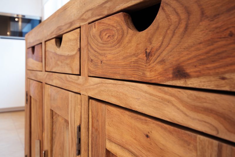Close-up of a wooden cabinet with multiple drawers, showing rich grain patterns and circular cut-out handles.
