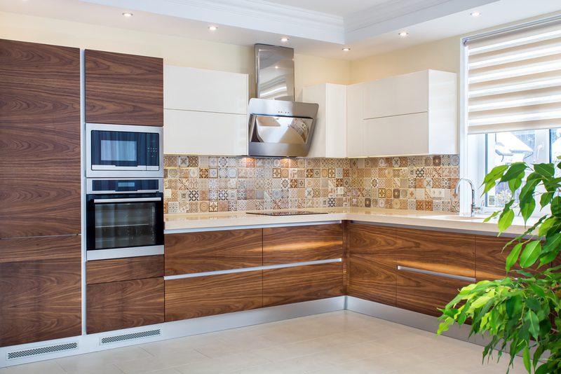 Modern kitchen with dark wood lower cabinets, white uppers, tiled backsplash, built-in oven and microwave, stainless hood, and a window with a plant.
