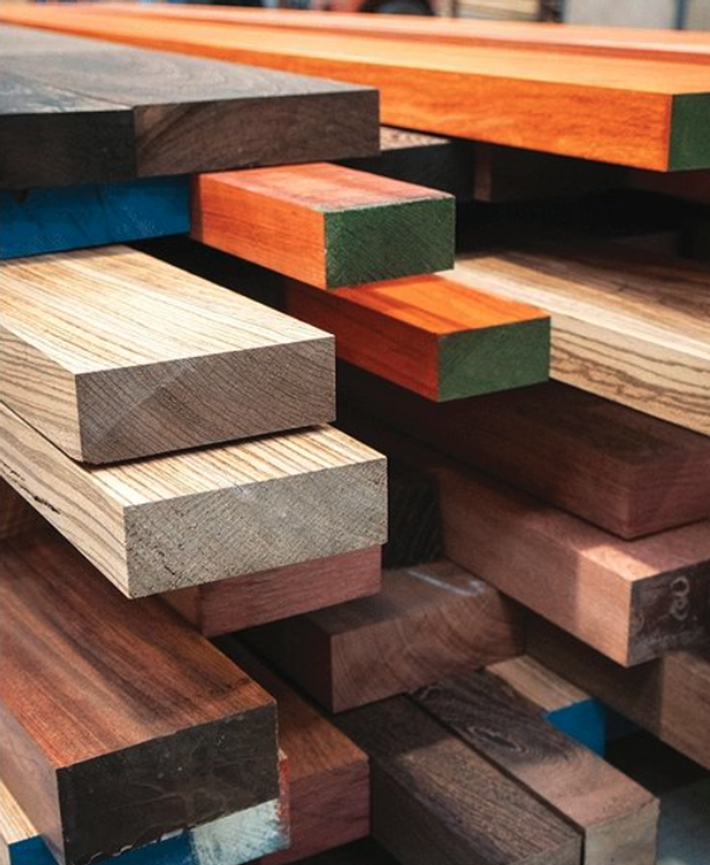 Stack of wooden planks in various colors with exposed ends; natural wood tones alongside blue, orange, and green accents.