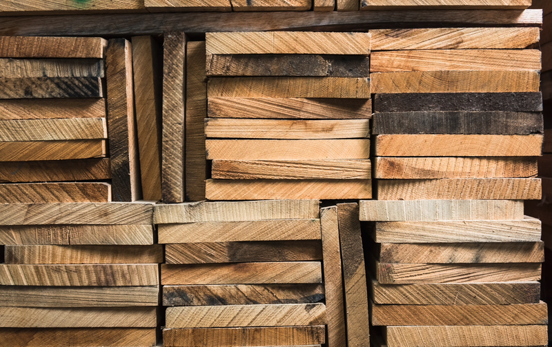Close-up of stacked wooden planks in varied widths and warm browns, showing grain patterns and rough edges.