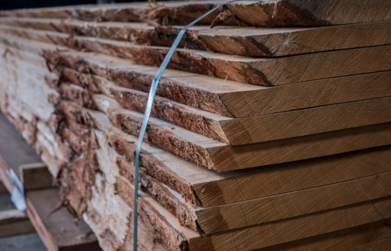 Stack of sawn wooden boards bound with a blue strap, exposing rough bark edges and visible wood grain.
