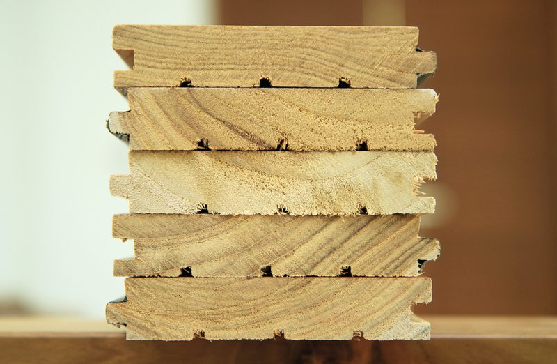 Stack of light wooden slats with notched edges, stacked in a neat column; visible wood grain against a blurred brown background.