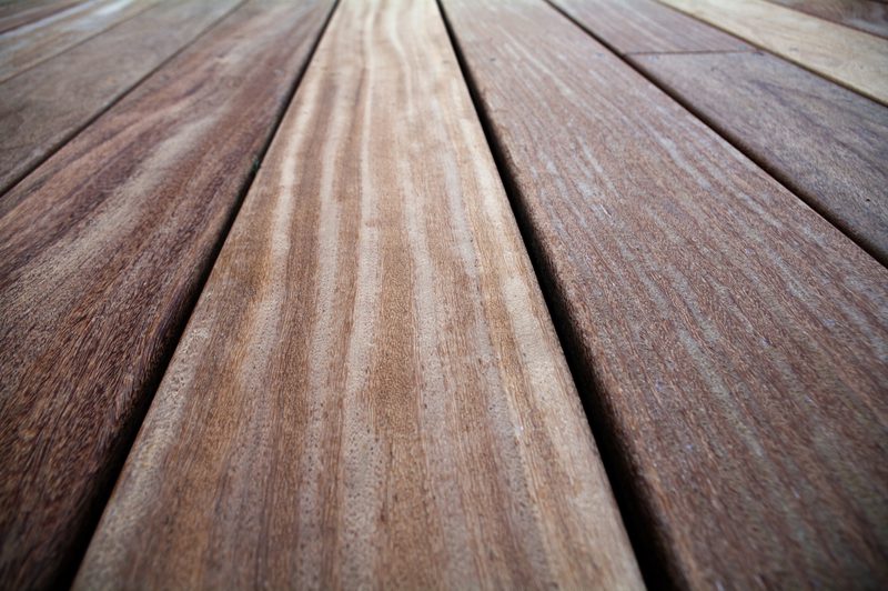 Close-up of wooden deck boards in warm brown tones, with visible grain patterns and parallel planks receding into the distance.