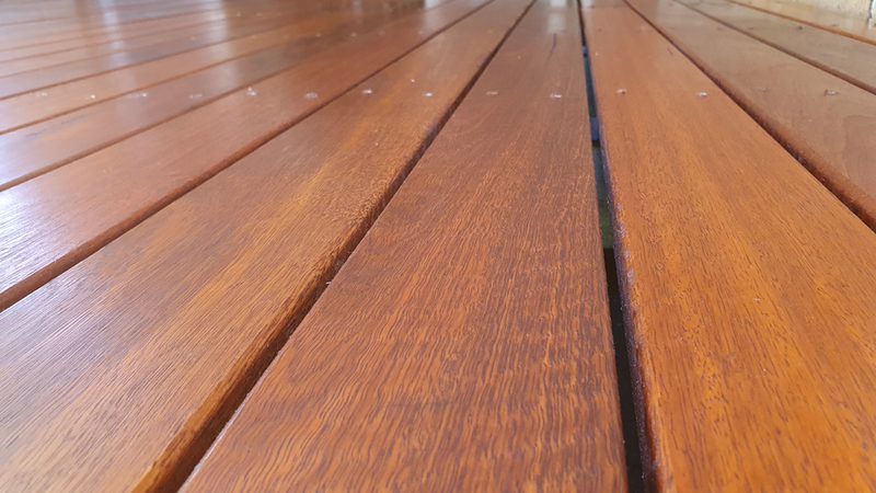 Close-up of polished wooden deck boards with visible grain in warm brown tones, laid in parallel lines receding into the distance.
