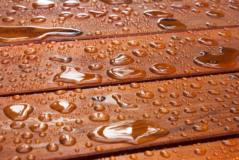 Close-up of brown wooden planks covered with water droplets of varying sizes, creating a glossy, reflective pattern.