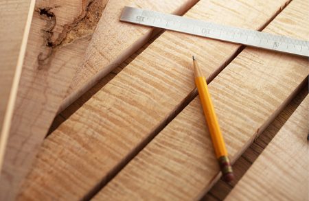 Close-up of light wood planks with a yellow pencil and a metal ruler laid diagonally across them.