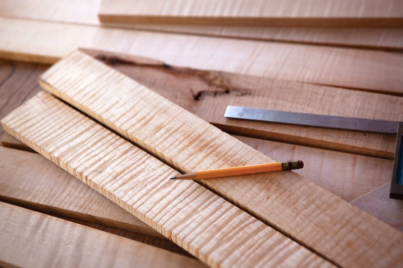 Light-colored wooden boards stacked on a workbench with a pencil and a metal ruler resting on top.