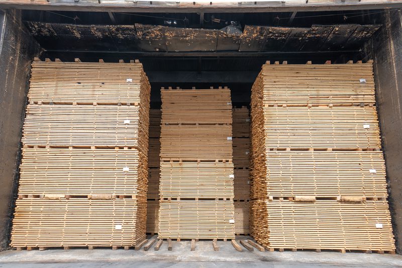 Inside a dark truck trailer, tall stacks of light wooden pallets arranged in three large piles with a central gap.