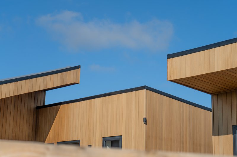Modern wooden building with vertical tan panels and dark trim under a clear blue sky.
