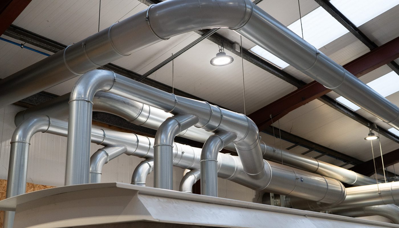 A network of shiny metal pipes running across the ceiling of a factory, leading to a large industrial extractor.