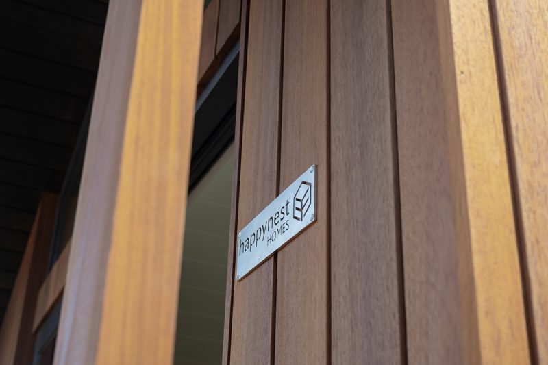 Wooden wall with vertical planks and a metal plaque reading 'happynest HOMES' beside a window.