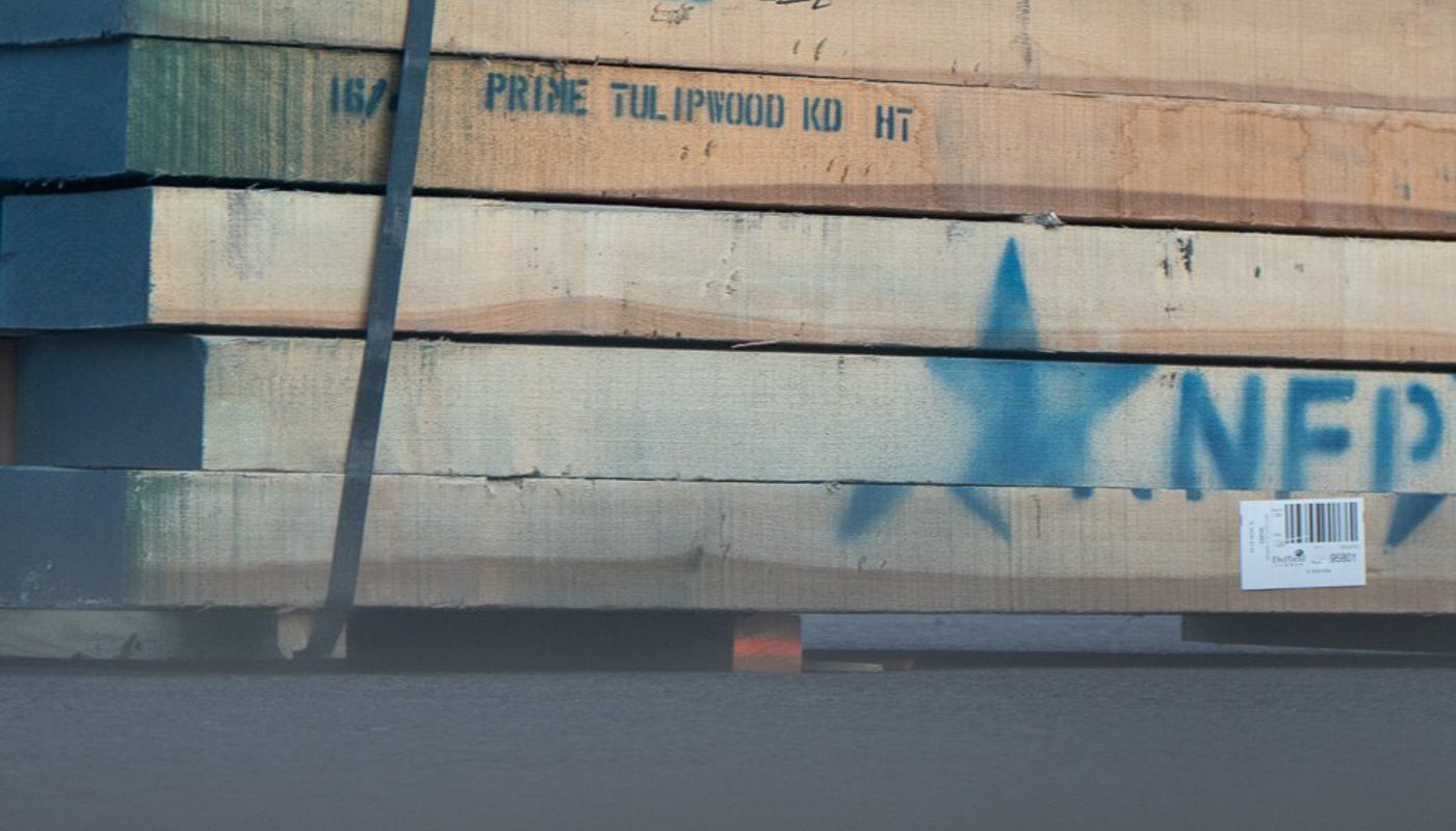 Stacked wooden lumber planks bound by a strap, light-brown boards with a blue spray-painted star/mark and a barcode sticker.