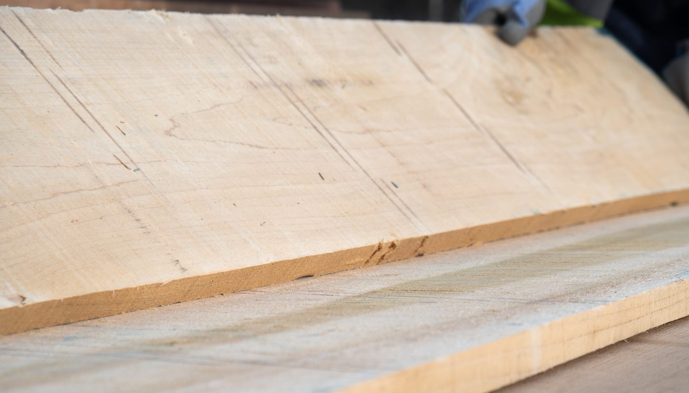 Two large plywood boards with visible grain and rough edges lie on a dusty wooden workbench, angled as if being prepared for cutting.